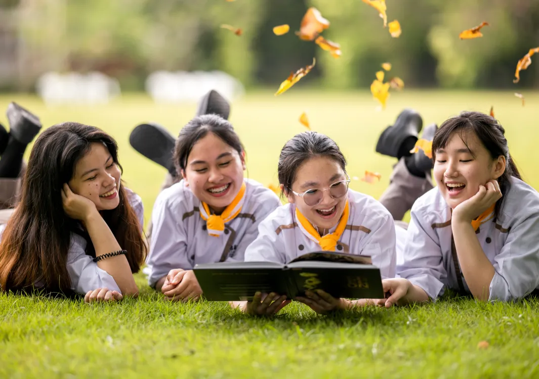 Students laughing and reading a book together on the grass